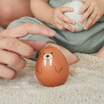 A close up pf an adult's hand reaching for the PlanToys walrus wobbly toy. A child can be seen in the background holding on to the PlanToys seal wobbly toy.