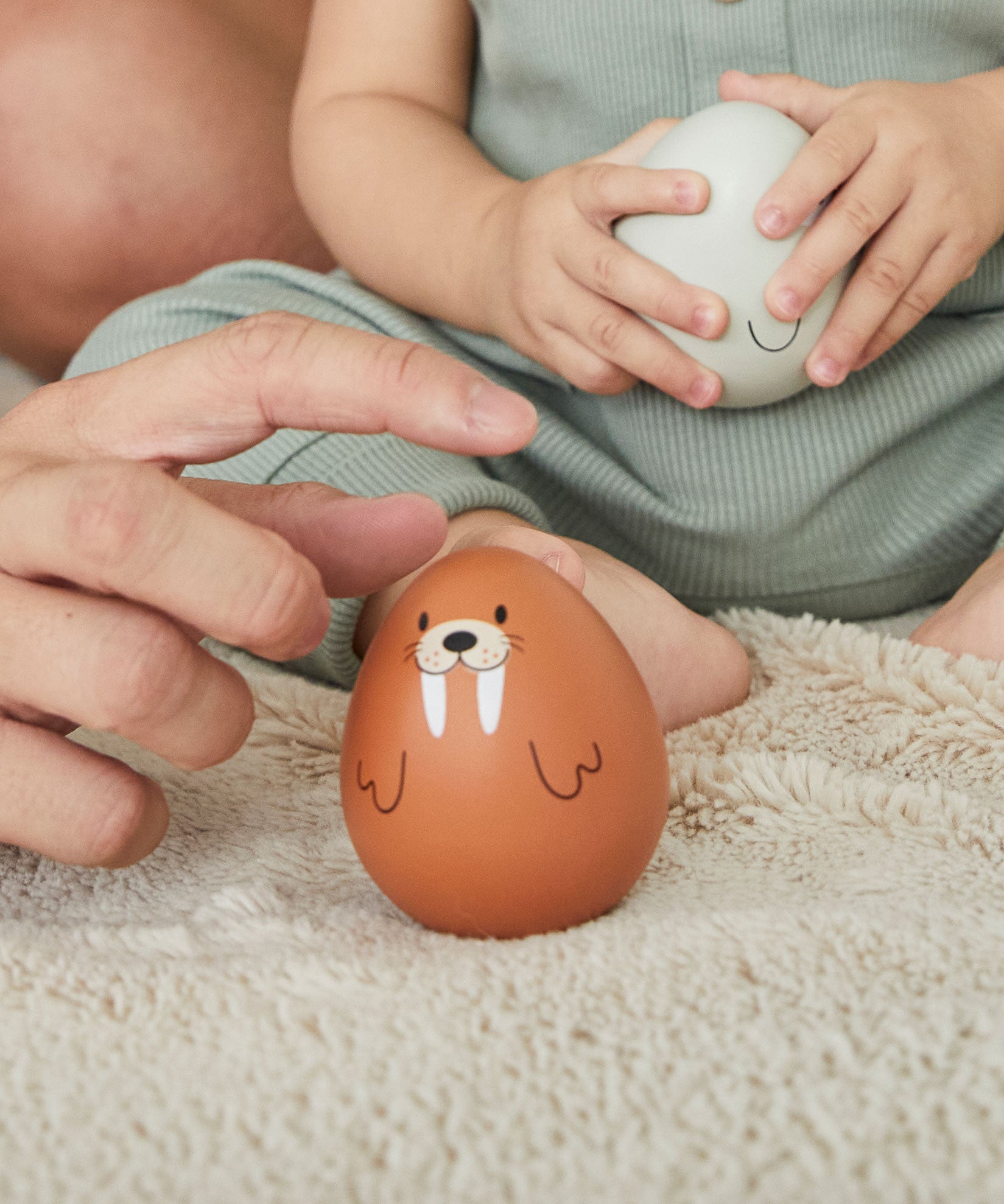 A close up pf an adult's hand reaching for the PlanToys walrus wobbly toy. A child can be seen in the background holding on to the PlanToys seal wobbly toy.