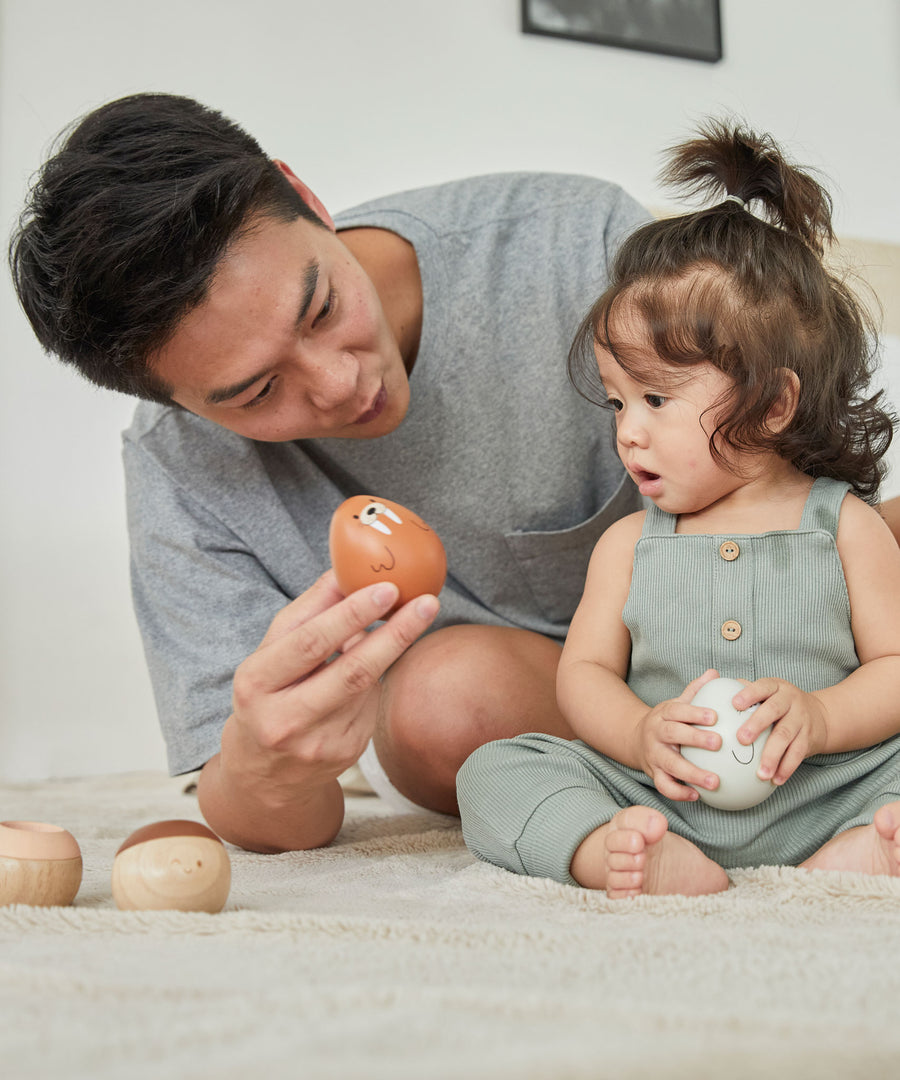 A young child and man sat on a fluffy carpet looking at the PlanToys plastic-free wobbly walrus toy.