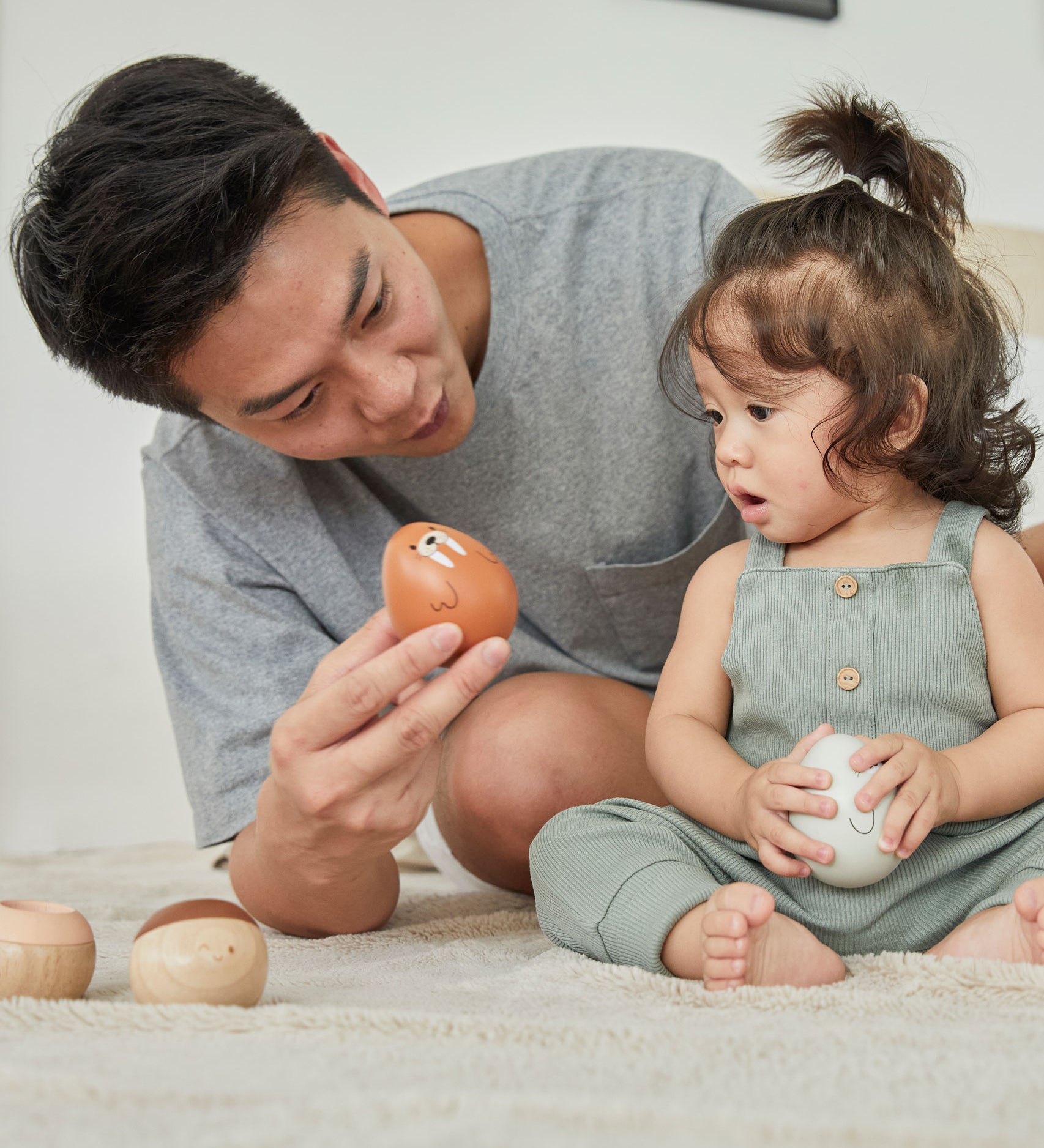 A young child and man sat on a fluffy carpet looking at the PlanToys plastic-free wobbly walrus toy.