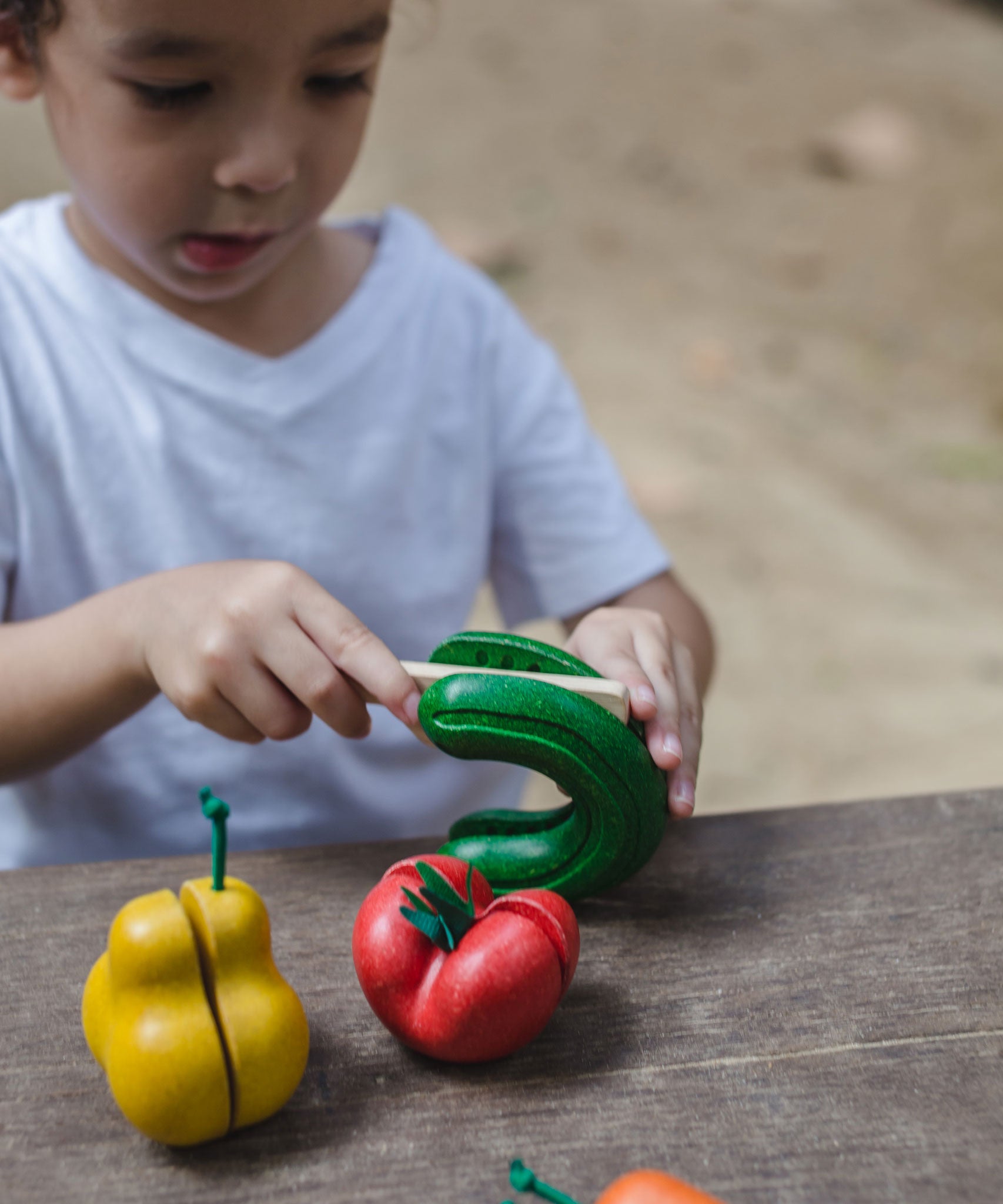 A child cutting up the toy cucumber from the PlanToys Wonky Fruit & Vegetables set. 