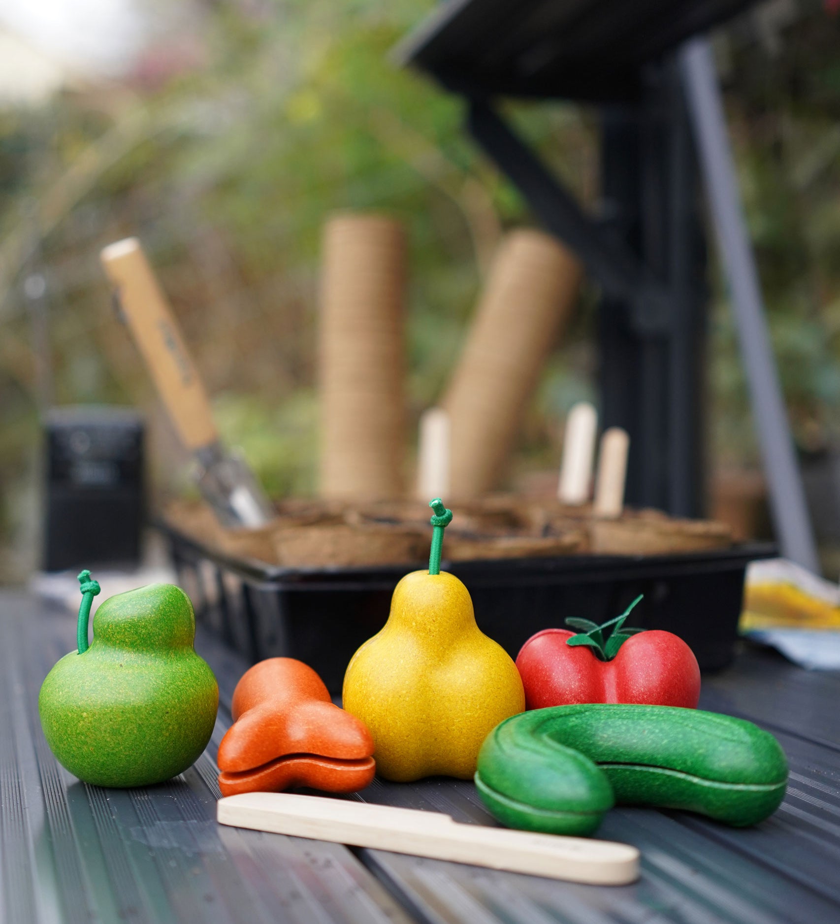 The PlanToys Wonky Fruit & Vegetables on a dark surface in a greenhouse. 