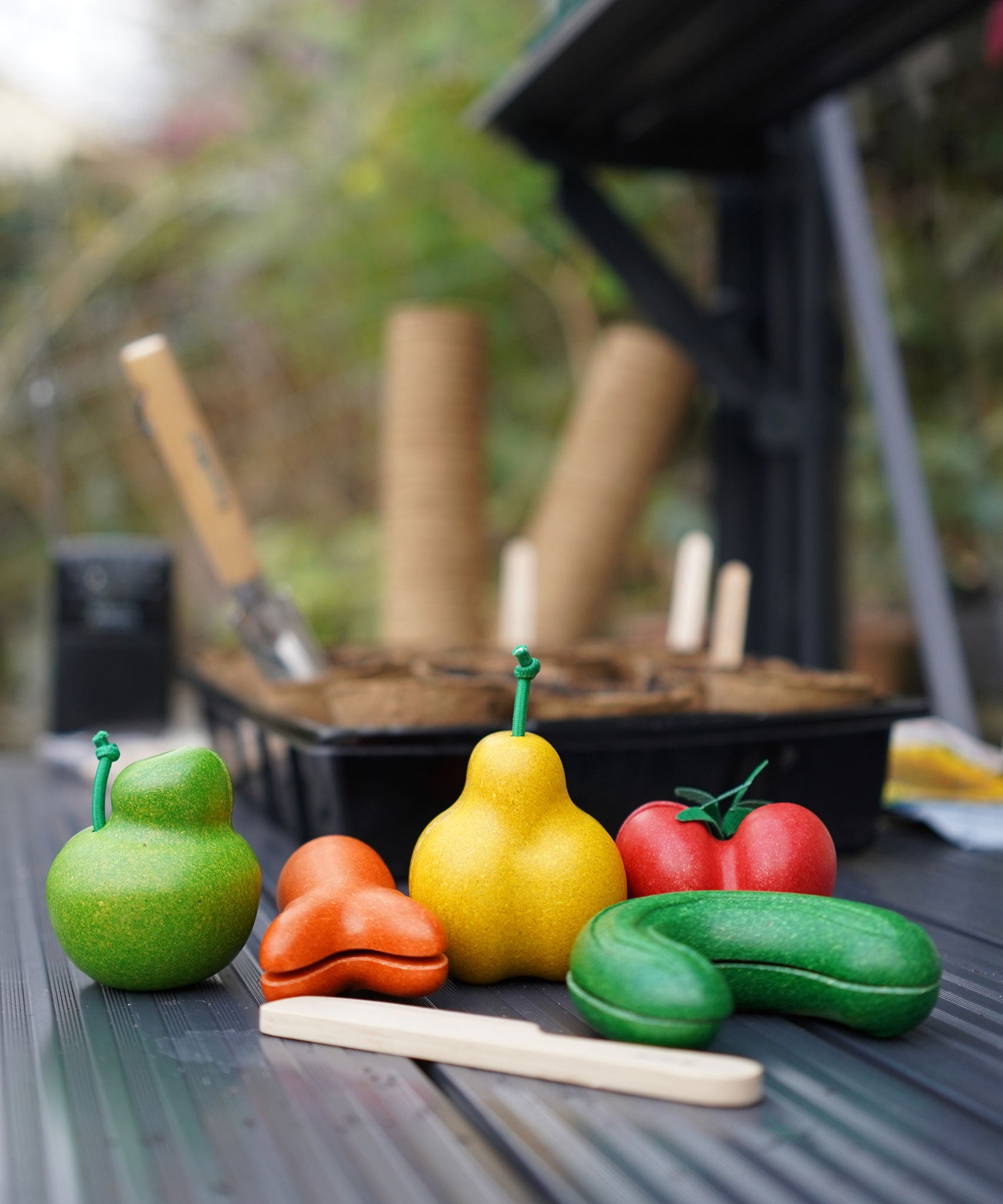 The PlanToys Wonky Fruit & Vegetables on a dark surface in a greenhouse. 