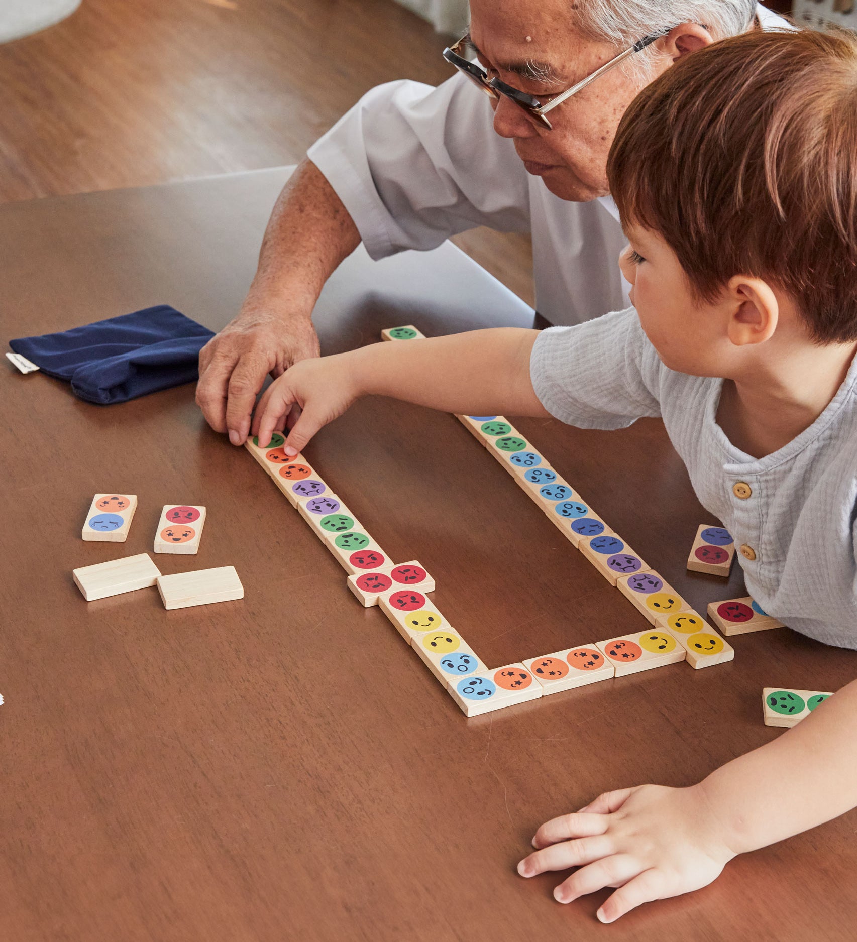 A child with an older man playing with the PlanToys wooden mood dominos game. 