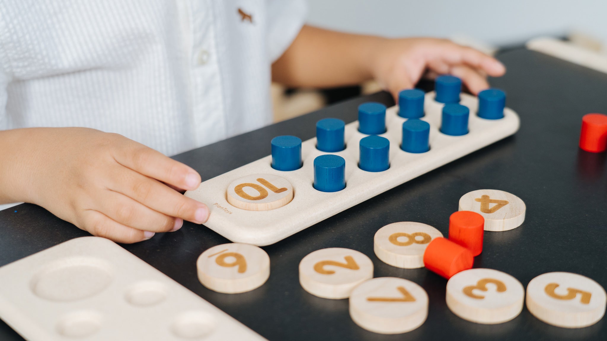 A close up of a child's hand playing with the PlanToys 10 Frame Number Game.