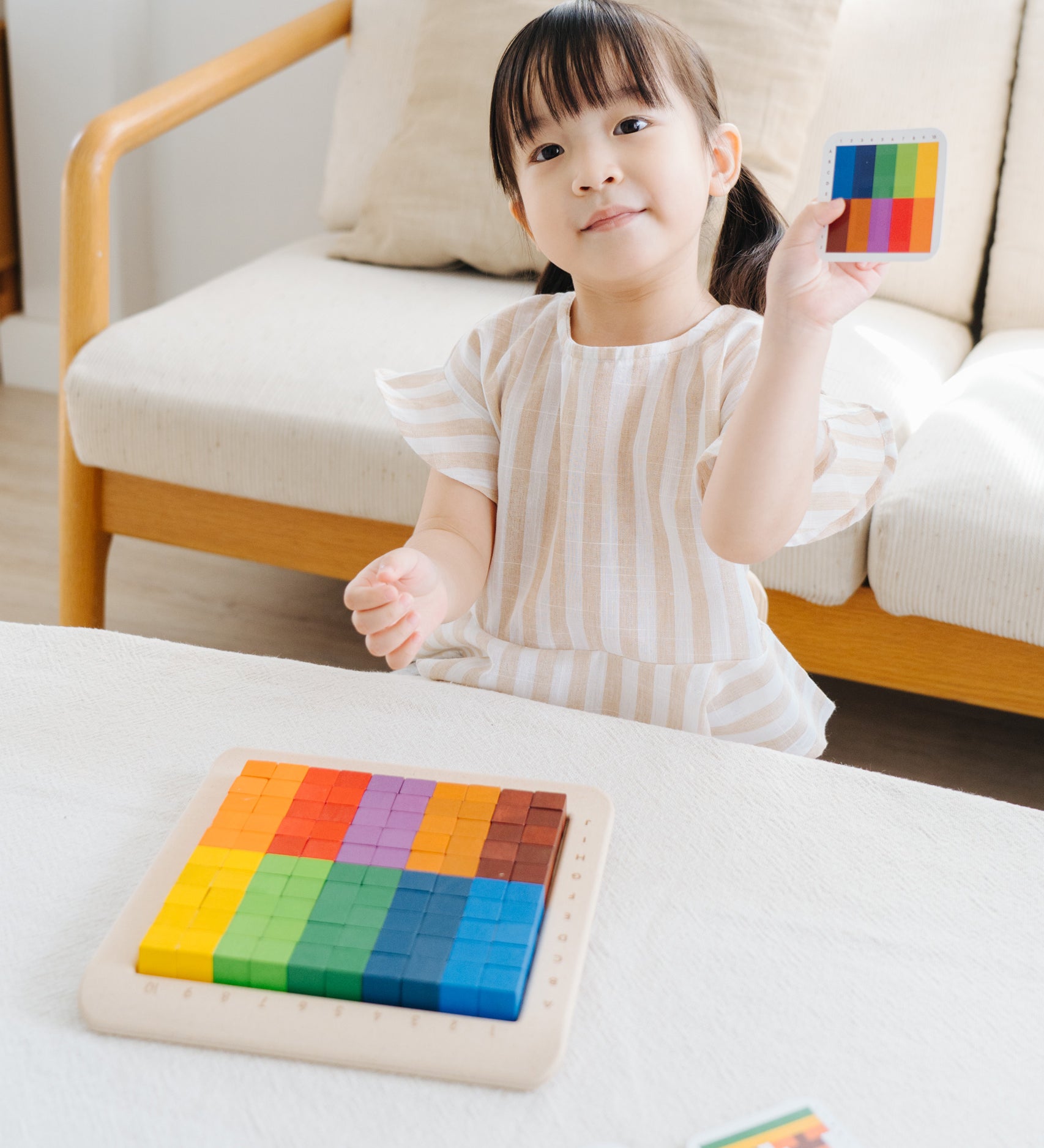 A child playing with the PlanToys 100 Rainbow Counting Cubes. The child is holding up one of the idea cards and has created the same pattern with the cubes. 