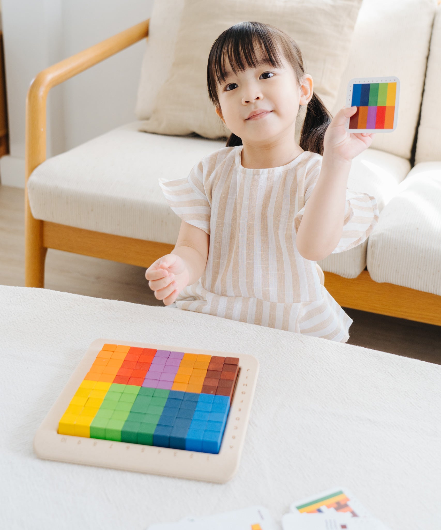 A child playing with the PlanToys 100 Rainbow Counting Cubes. The child is holding up one of the idea cards and has created the same pattern with the cubes. 