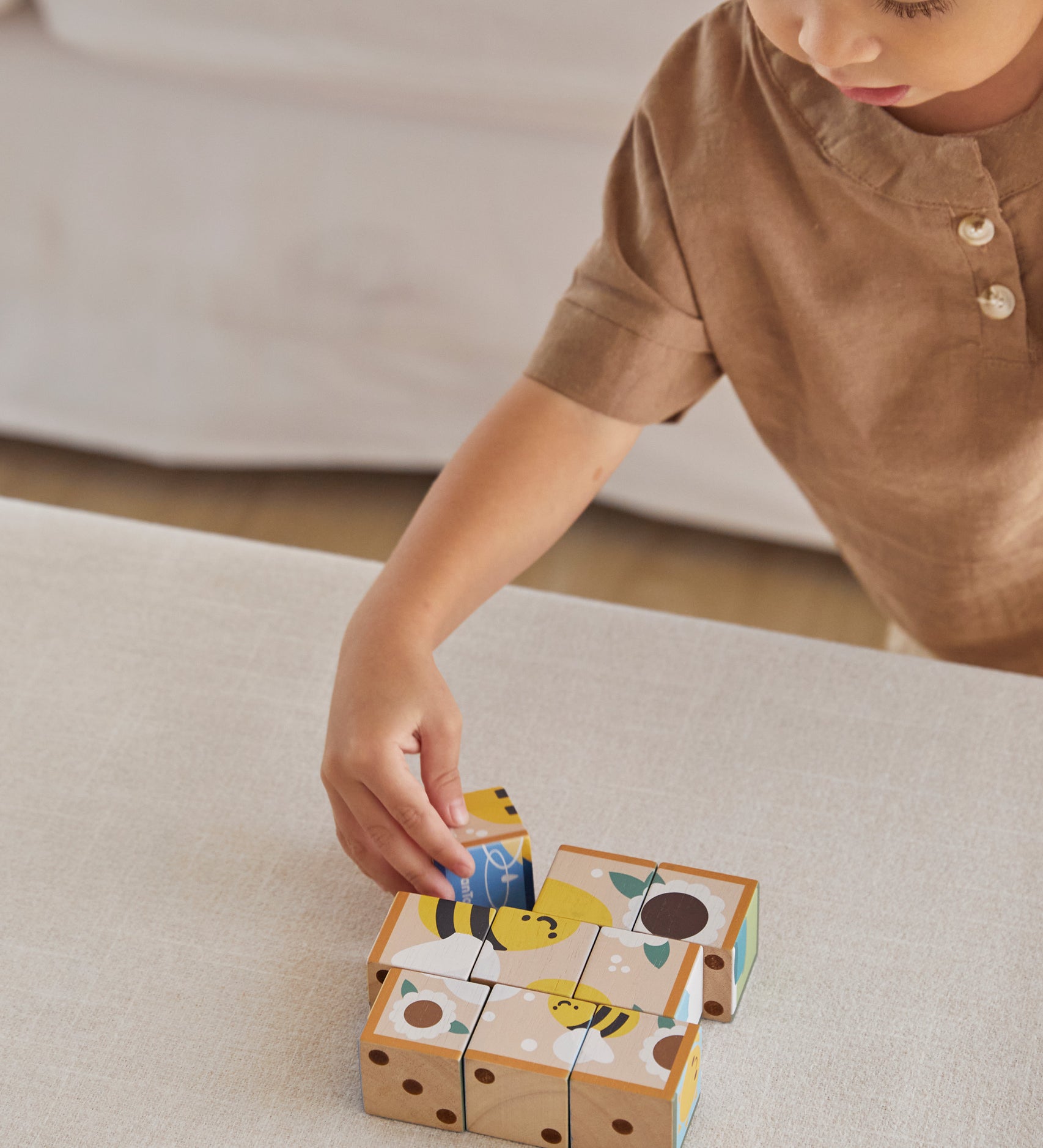 A child playing with the PlanToys Wooden Animal Puzzle Cubes, they are placing the blocks to form the bee themed photo. 