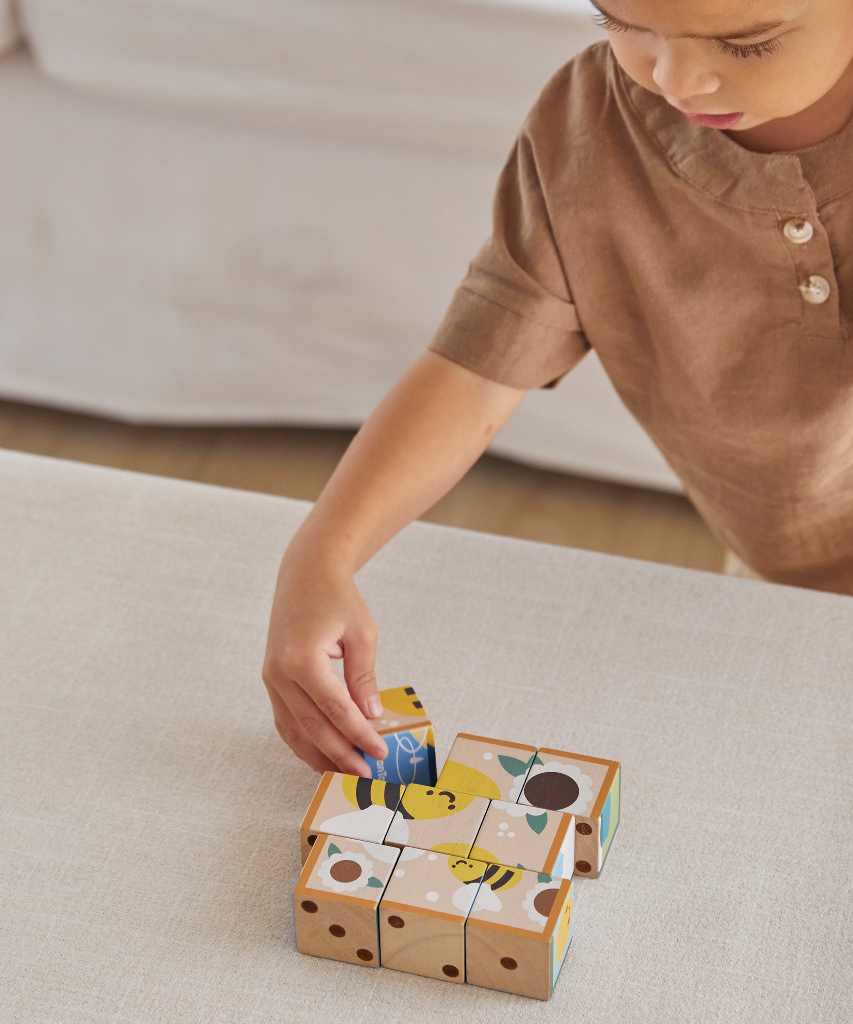 A child playing with the PlanToys Wooden Animal Puzzle Cubes, they are placing the blocks to form the bee themed photo. 