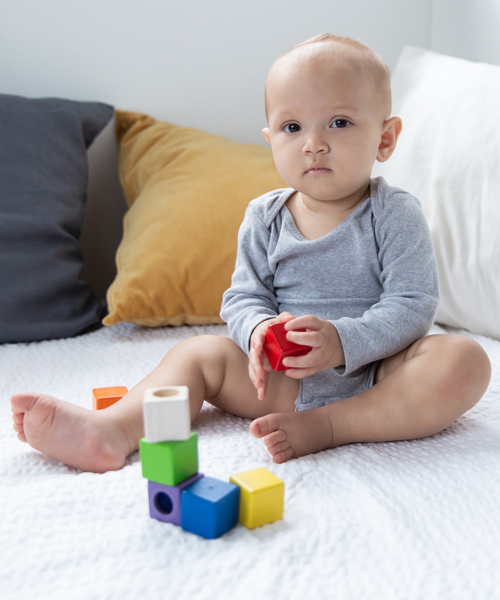 A baby sitting on a white blanket playing with the PlanToys kids wooden sensory activity blocks. 