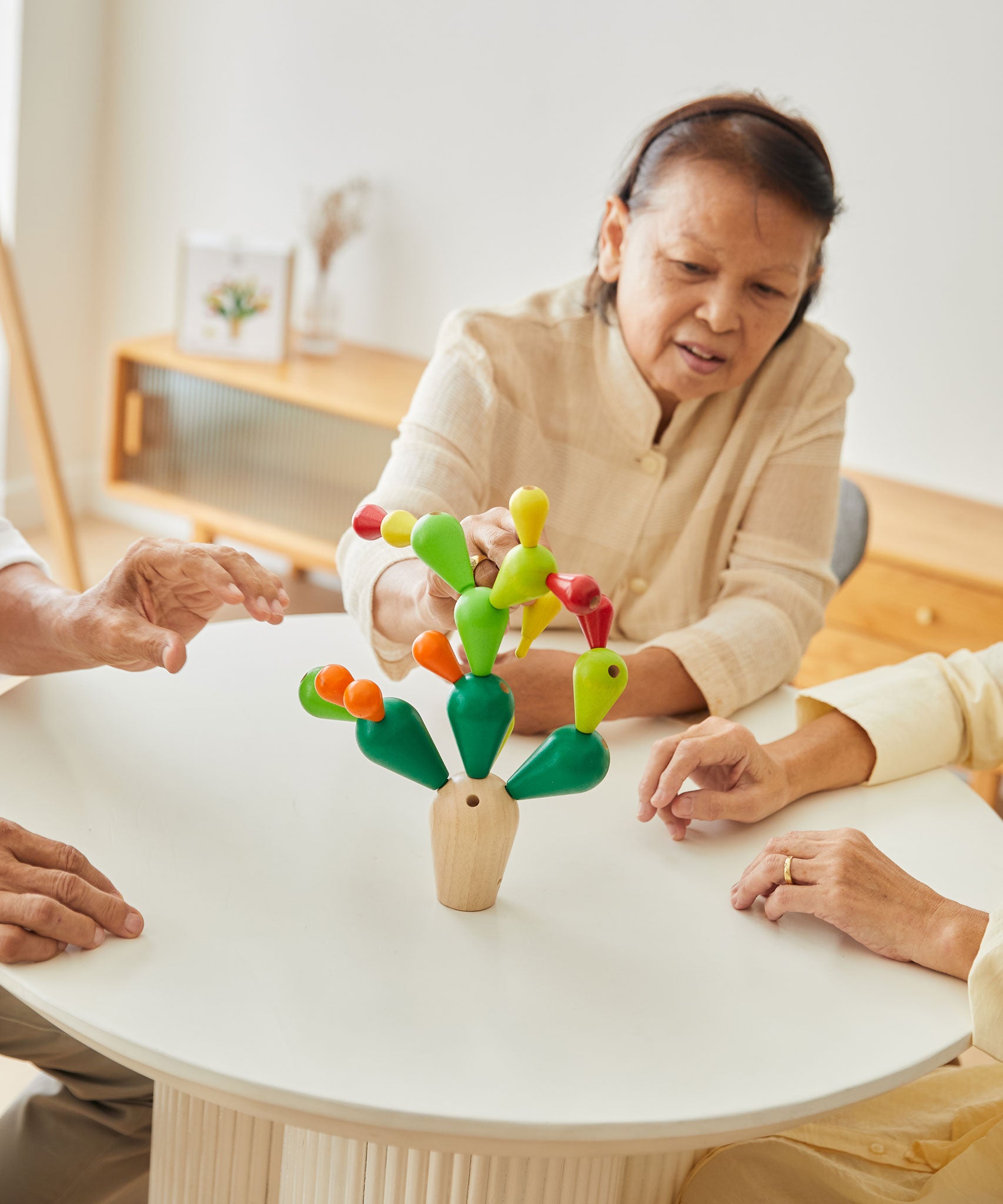 Three adults sitting around a table playing with the  PlanToys Balancing Cactus.