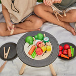 Close up of two children playing with some play food vegetables on top of the PlanToys BBQ role play set