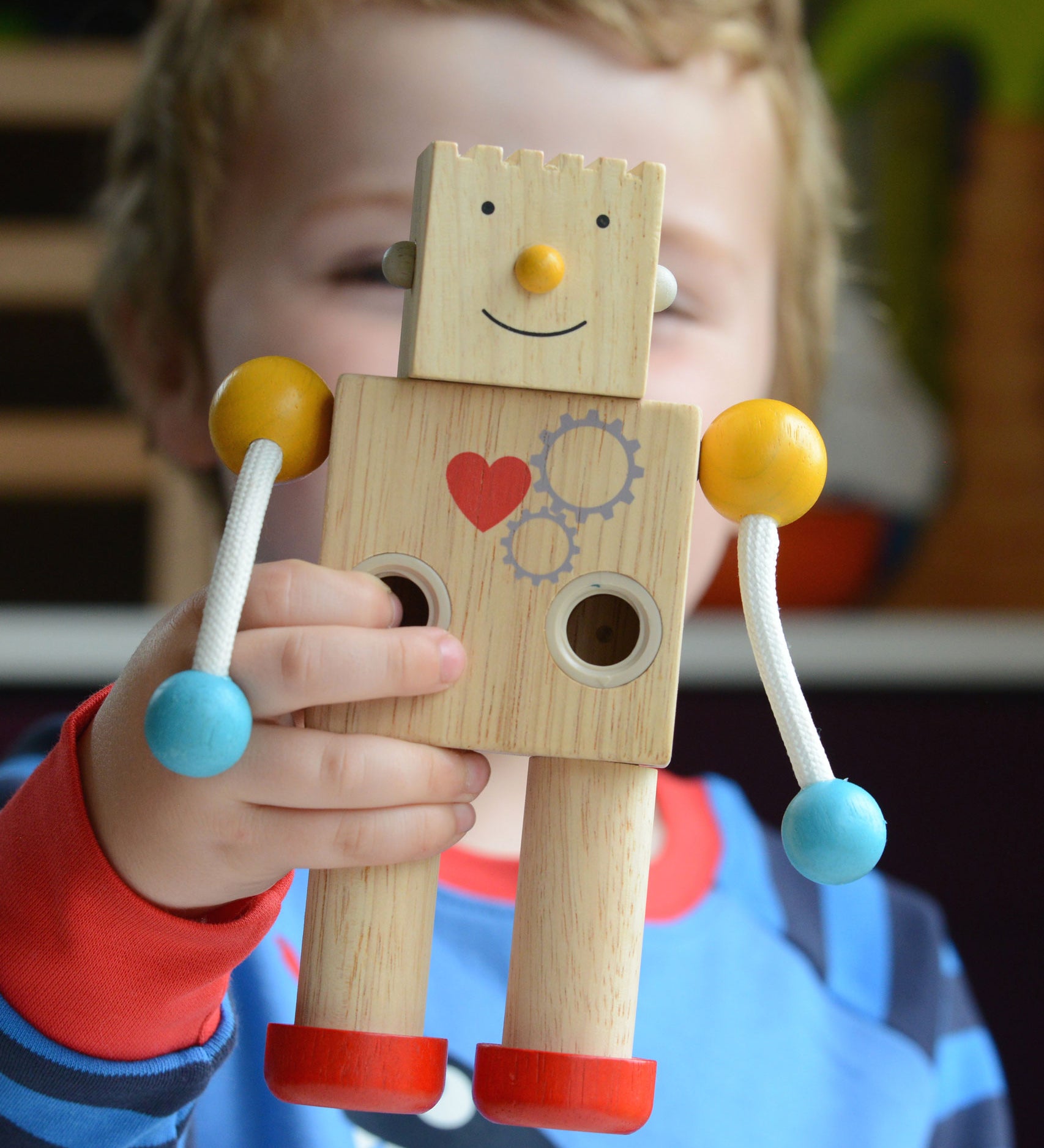 A close up of a child holding up a PlanToys Build a Robot toy. The robot has it's square shaped face on with a happy expression. 