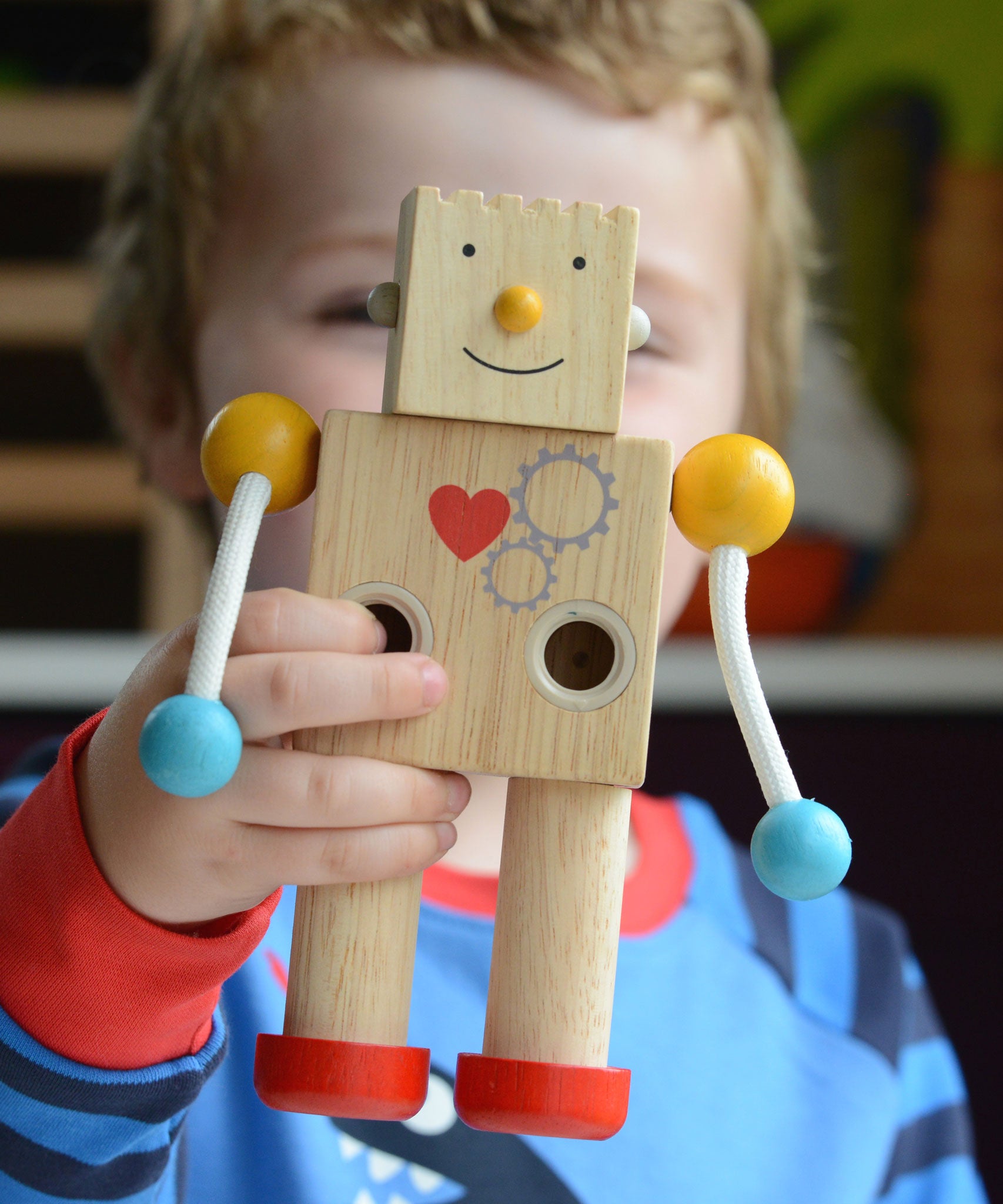 A close up of a child holding up a PlanToys Build a Robot toy. The robot has it's square shaped face on with a happy expression. 