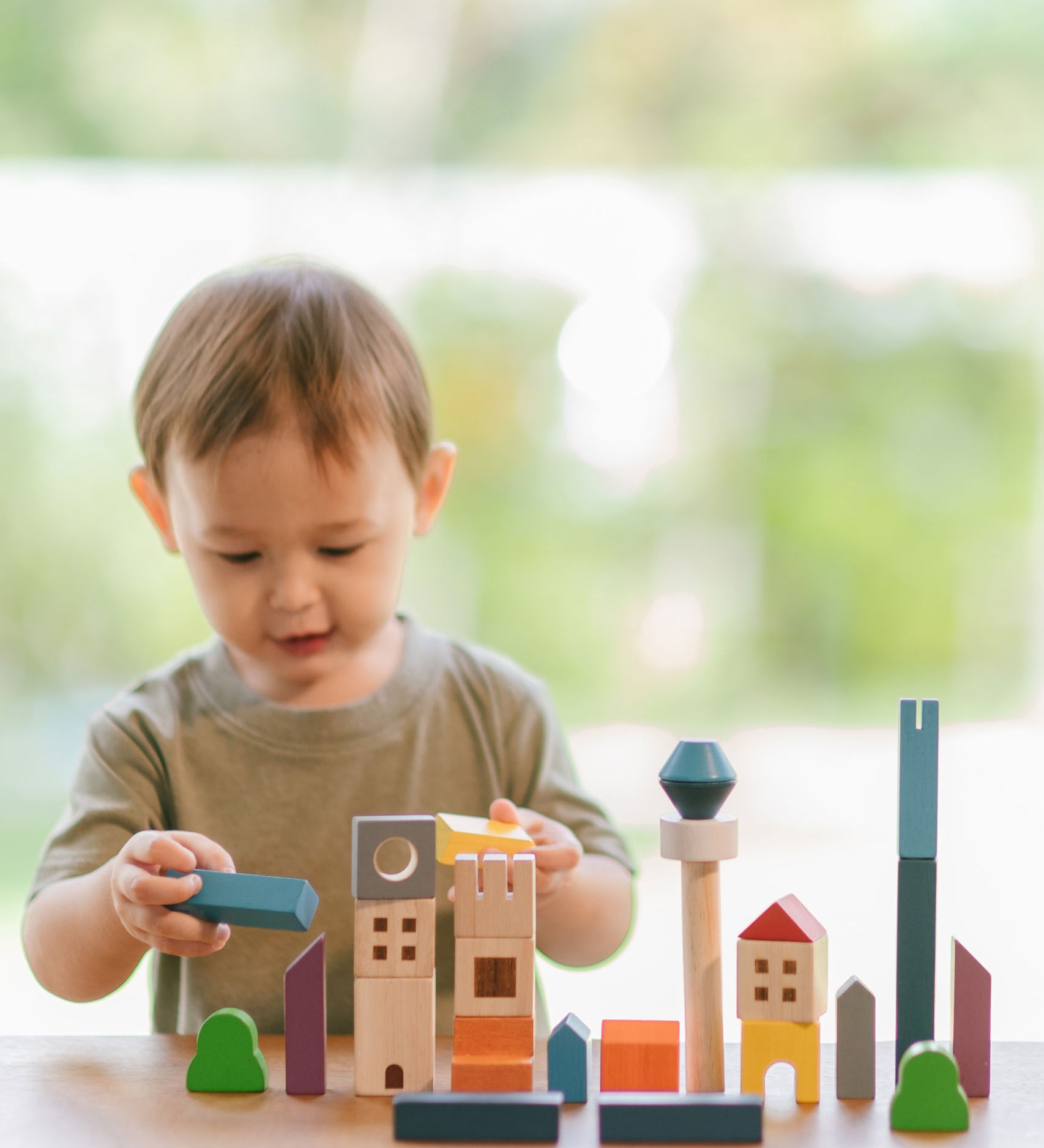 A child playing with the PlanToys Wooden Cityscape Blocks, the child is holding one of the blue blocks in one hand and a yellow one in the other. 