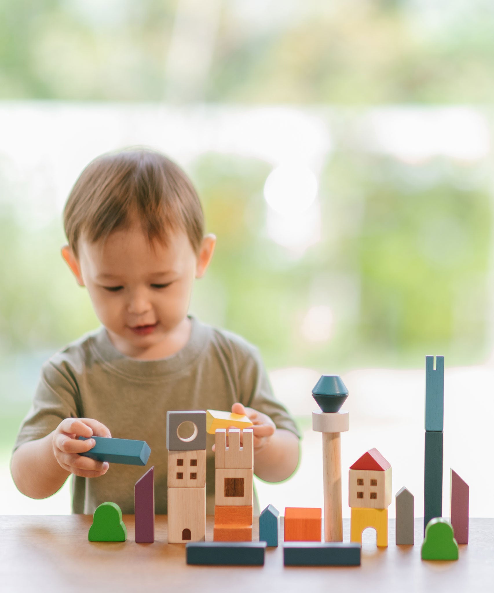 A child playing with the PlanToys Wooden Cityscape Blocks, the child is holding one of the blue blocks in one hand and a yellow one in the other. 