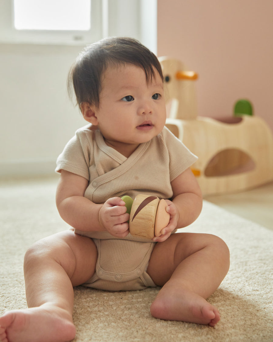 Young child sat on the floor holding the PlanToys plastic-free wooden sensory clapping roller toy. 