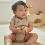 Young child sat on the floor holding the PlanToys plastic-free wooden sensory clapping roller toy. 