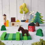 The PlanToys Wooden Country Blocks set up in a small world play set up, Bumbu trees can be seen in the background. 