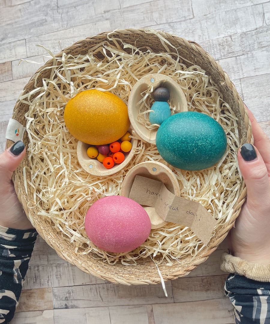 Three PlanToys Eggs in a basket each containing various little treasures. One has beads inside, one has a baby Nin and the third has handwritten little note.