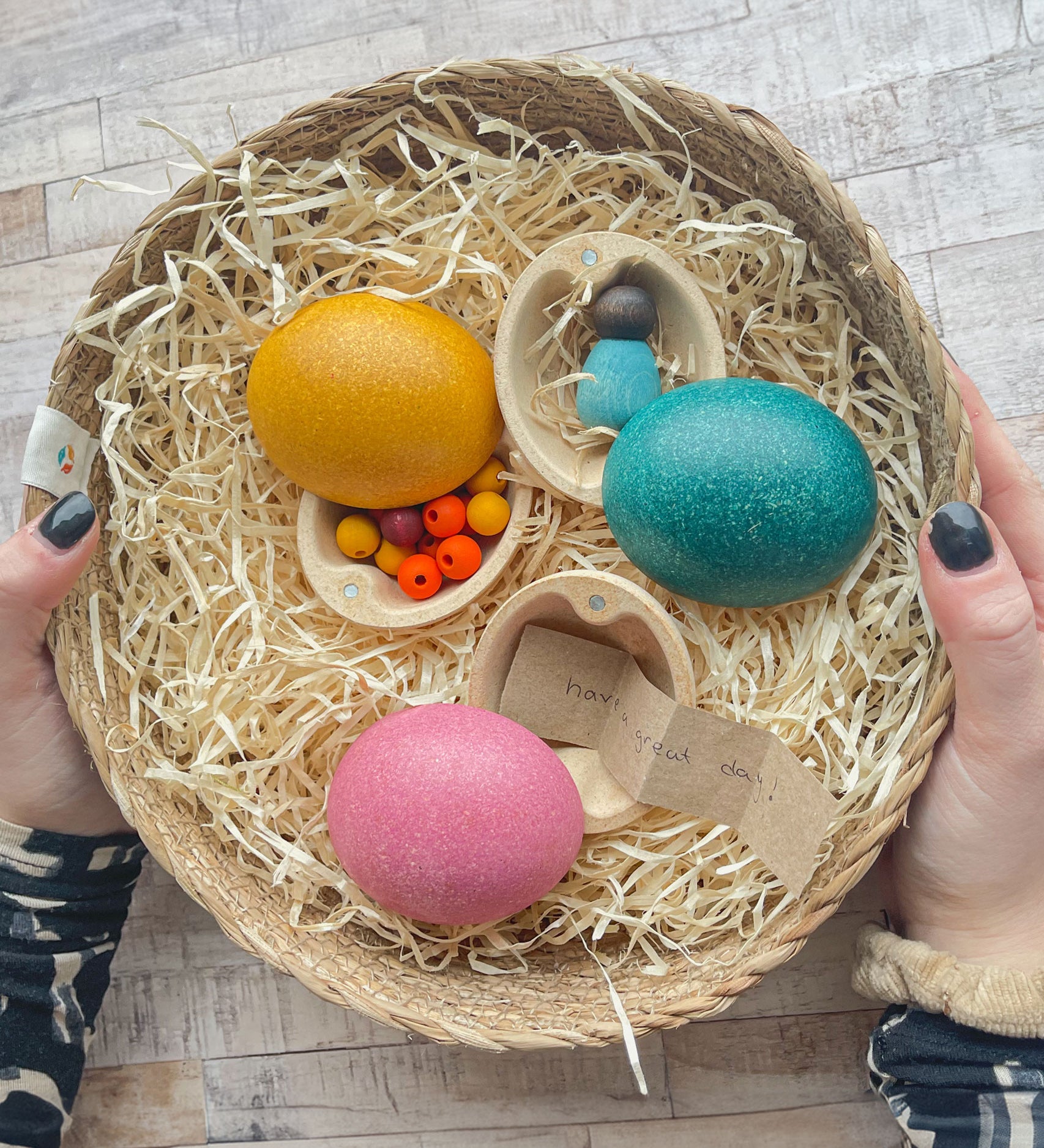 Three PlanToys Eggs in a basket each containing various little treasures. One has beads inside, one has a baby Nin and the third has handwritten little note.