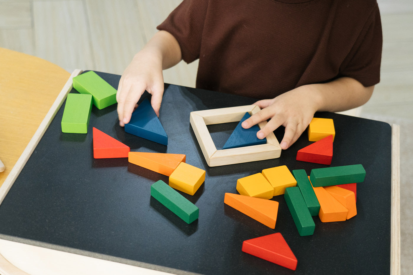 Close up of child's hands playing with the PlanToys solid wooden fraction blocks on a wooden table