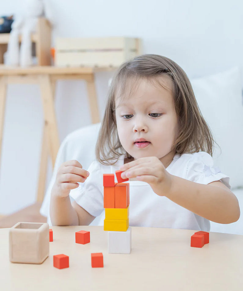 A child playing with the PlanToys Fractions Cubes. They are creating a stack. 