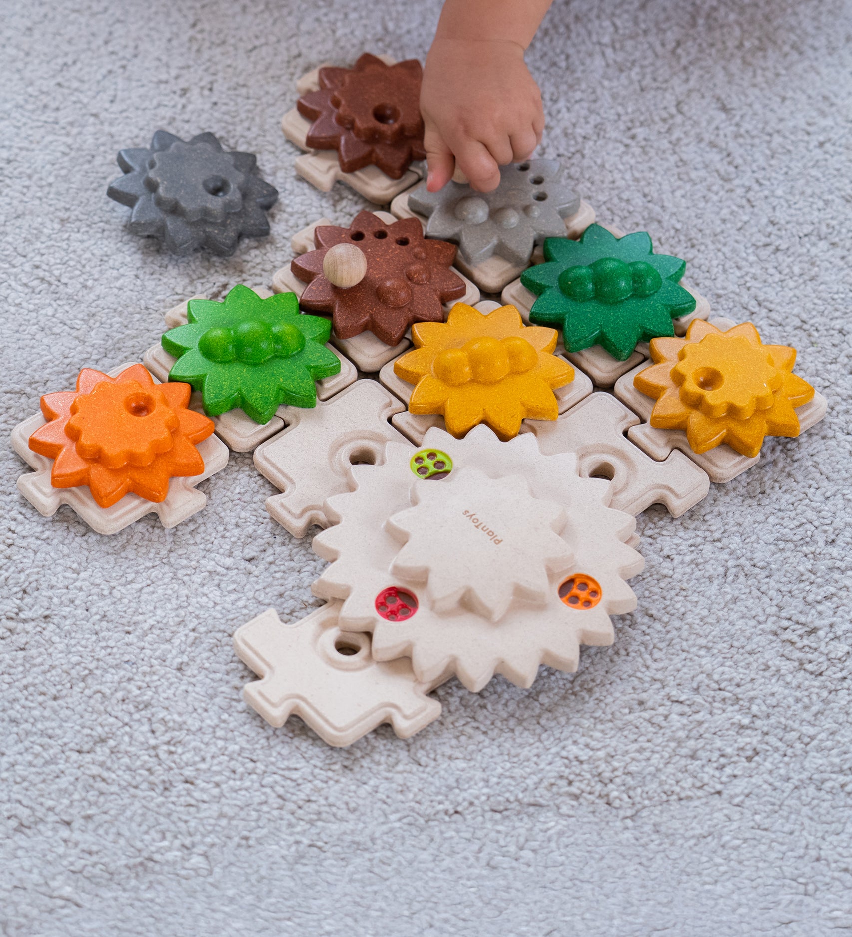 A close up of a child's hand playing with the PlanToys Gear and Puzzle. 