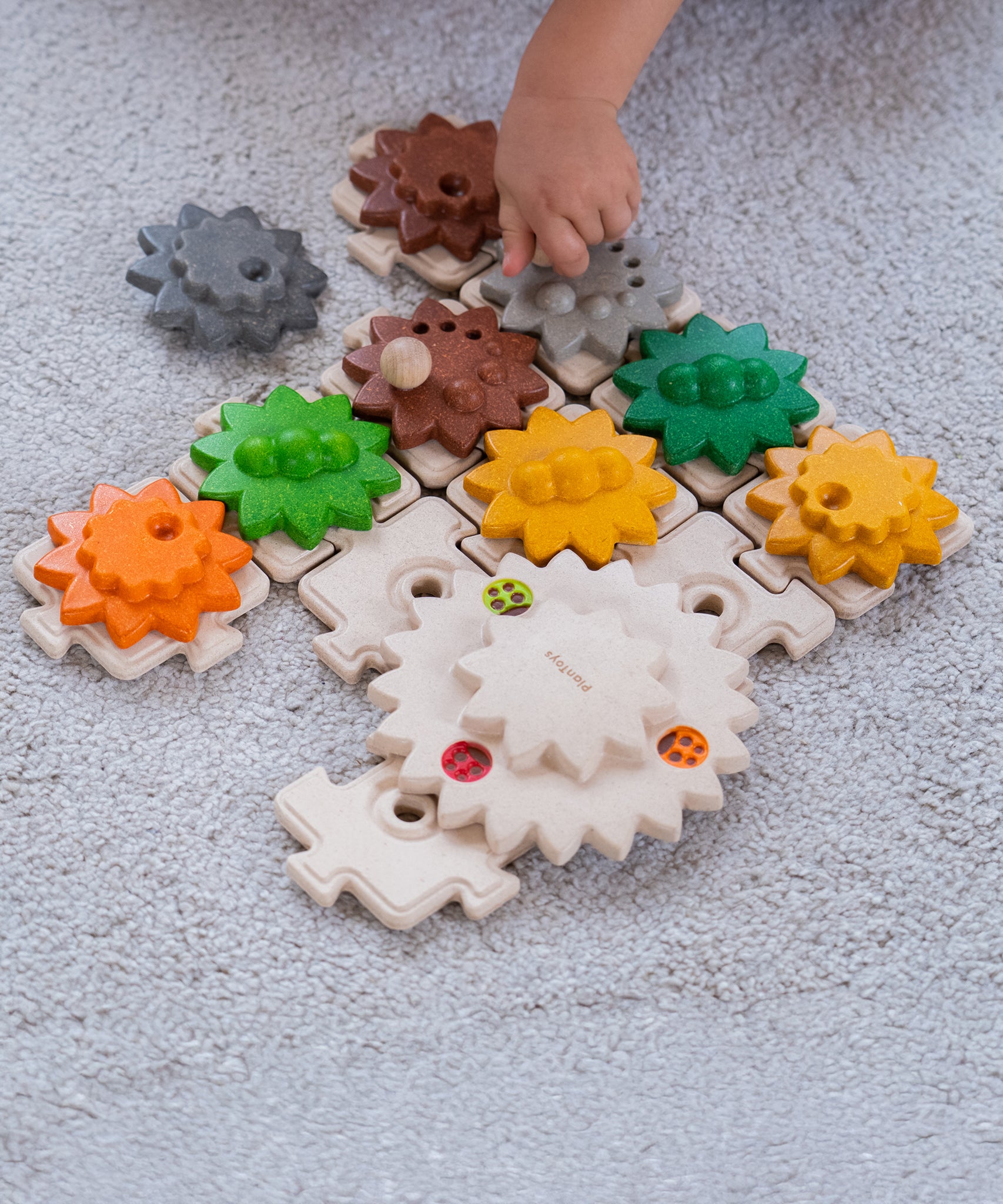 A close up of a child's hand playing with the PlanToys Gear and Puzzle. 