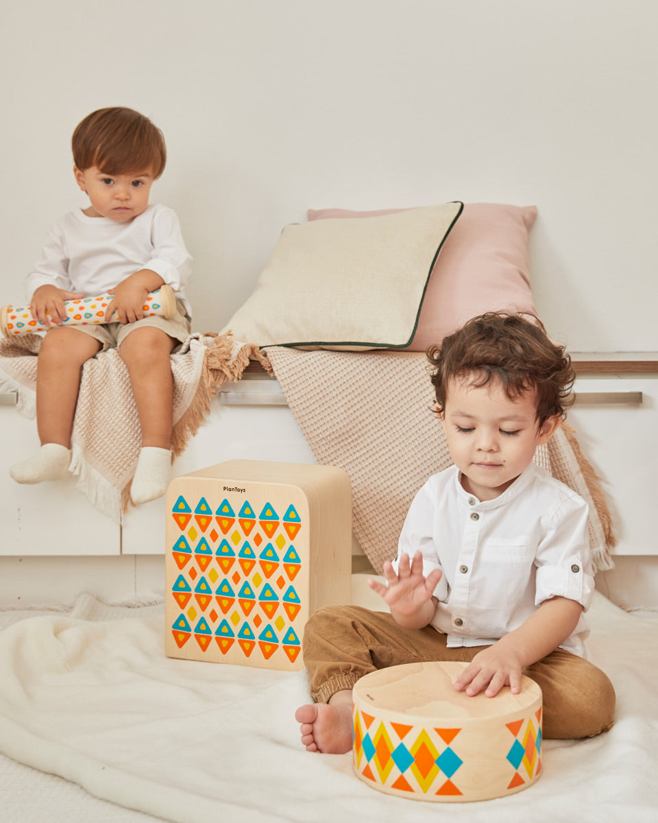 2 children sat down playing with the PlanToys solid wooden musical drum toy