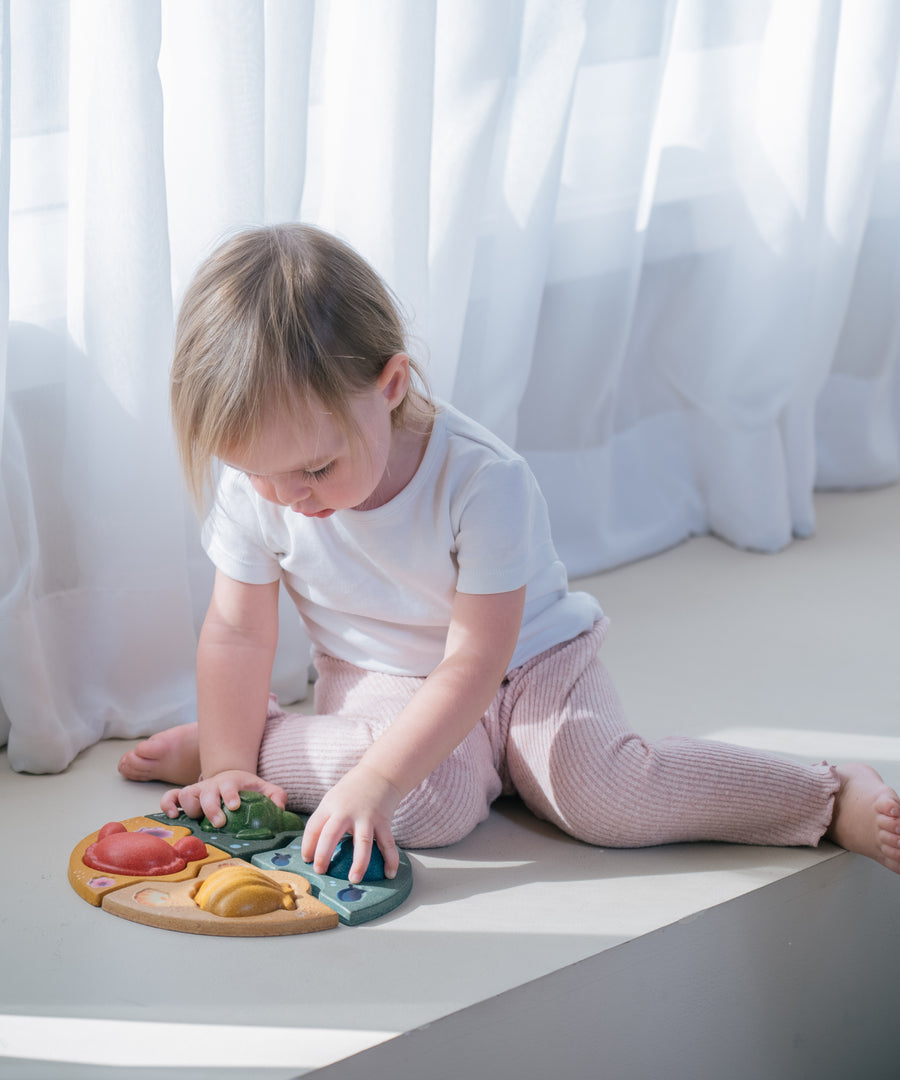 A child sitting on the floor playing with the PlanToys Marine Puzzle.