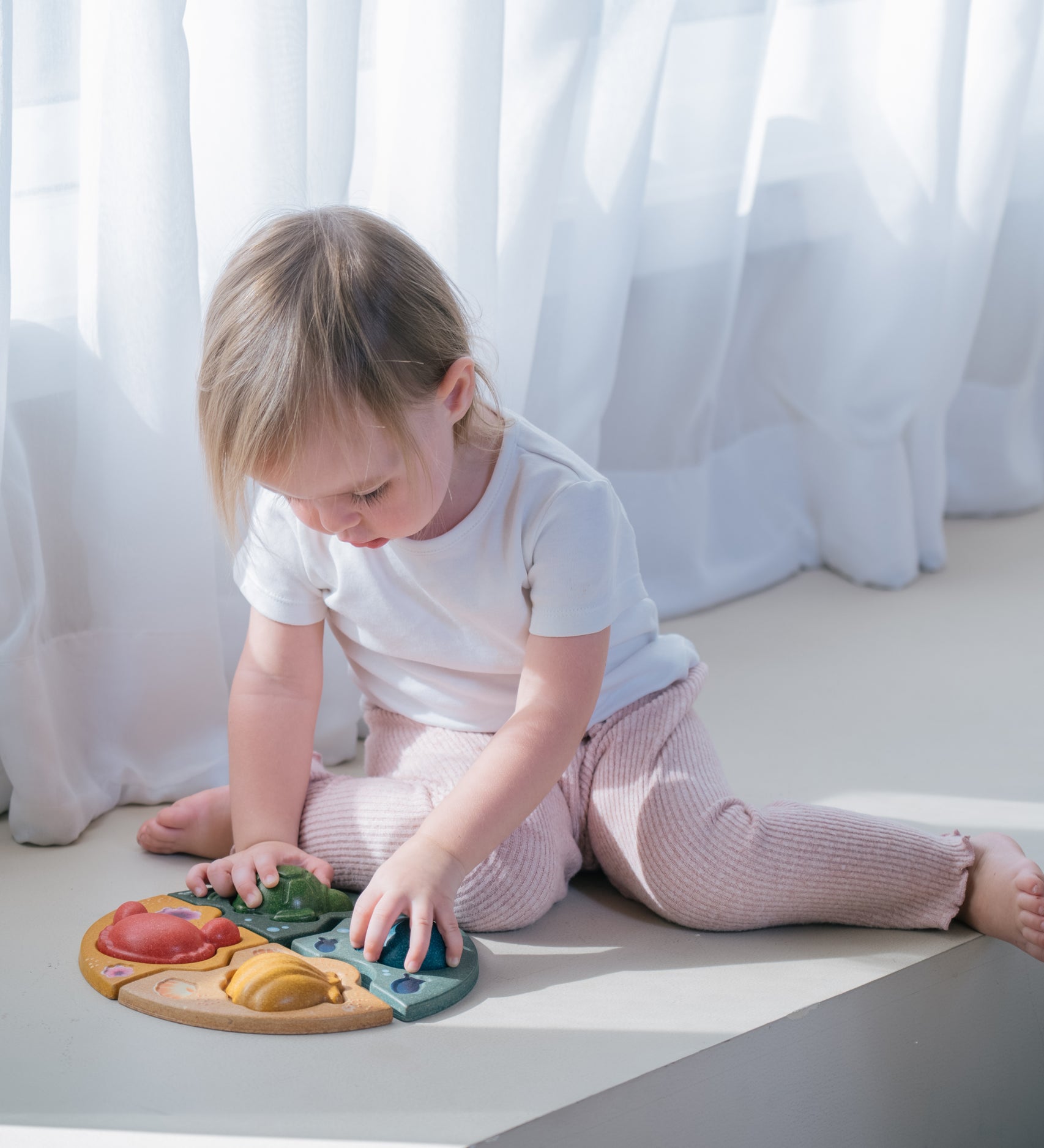 A child sitting on the floor playing with the PlanToys Marine Puzzle.