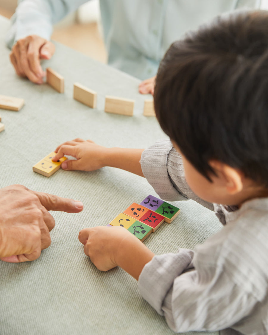 Close up of young boy putting down a piece of the PlanToys mood dominos set on a table