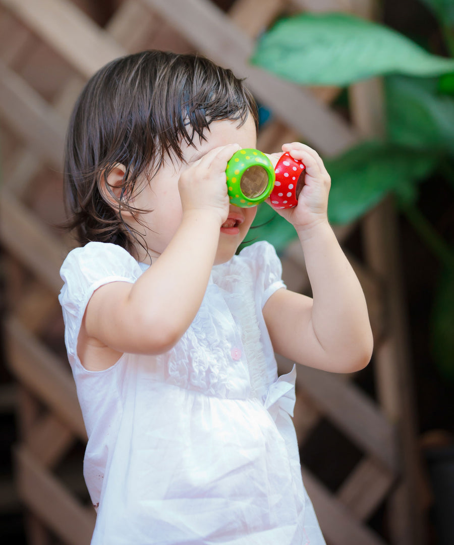 A child holding the green and red PlanToys Mushroom Kaleidoscope up to their eyes. 