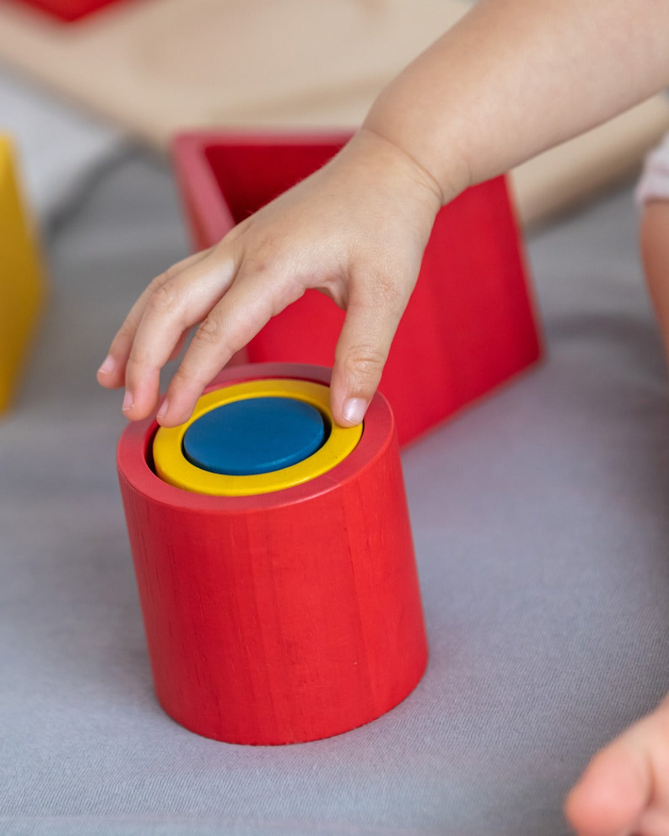 Close up of young child making a stack with the PlanToys matching and nesting shapes on a grey bed