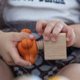 A close up of a child twisting PlanToys Wooden Nuts and Bolts Orange Tap Handle into a wooden block.