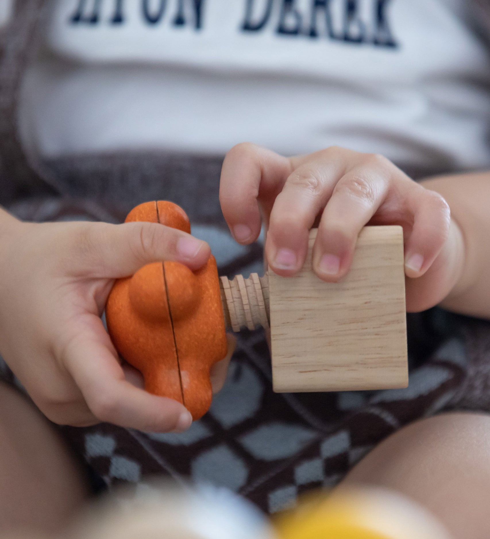 A close up of a child twisting PlanToys Wooden Nuts and Bolts Orange Tap Handle into a wooden block.