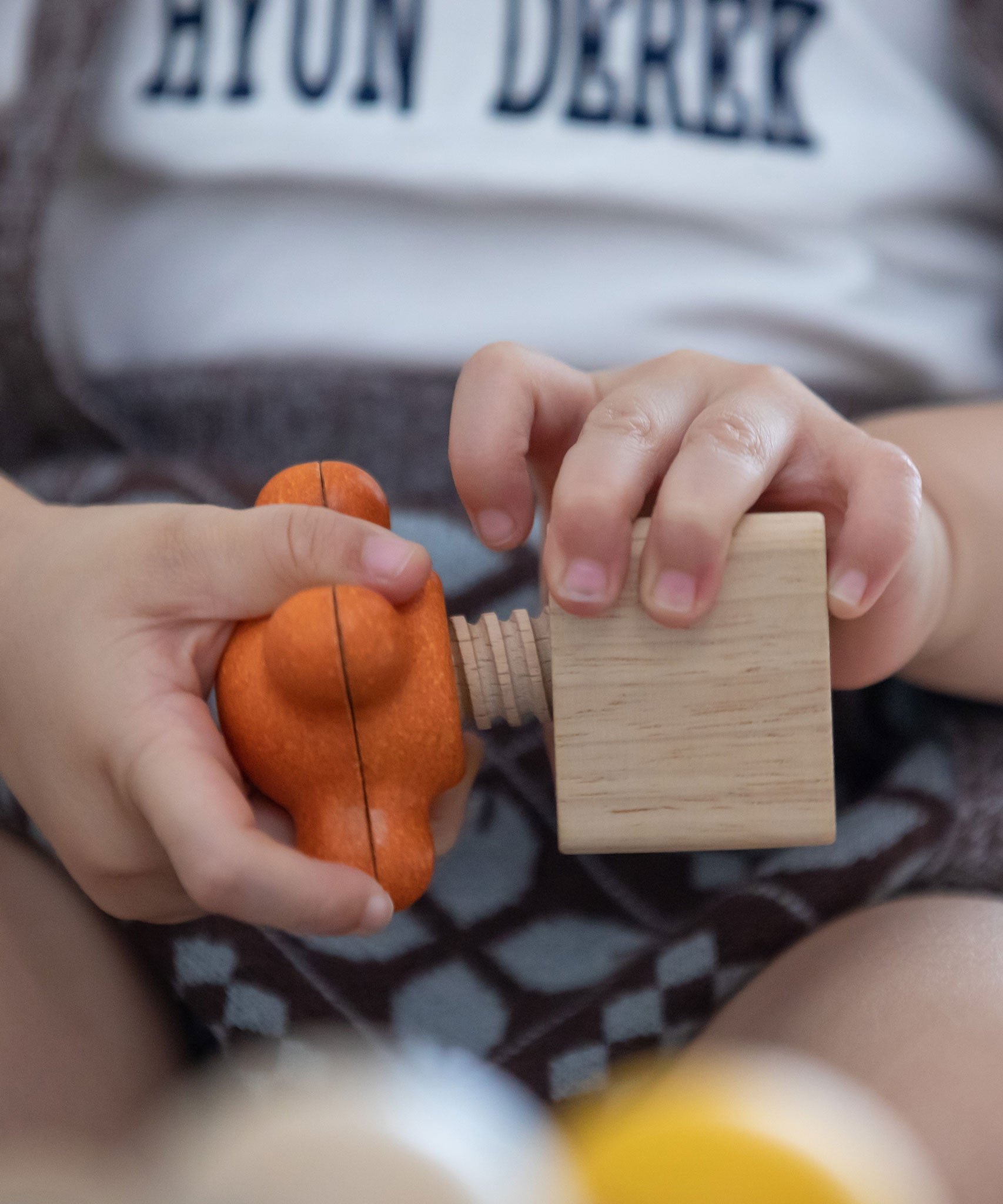 A close up of a child twisting PlanToys Wooden Nuts and Bolts Orange Tap Handle into a wooden block.