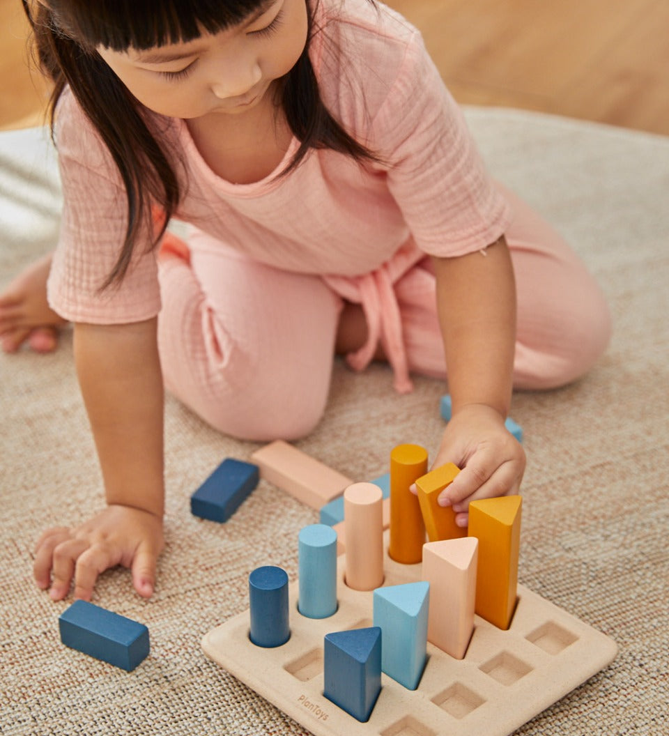 Young child crouched down placing shapes in the PlanToys wooden orchard peg board toy