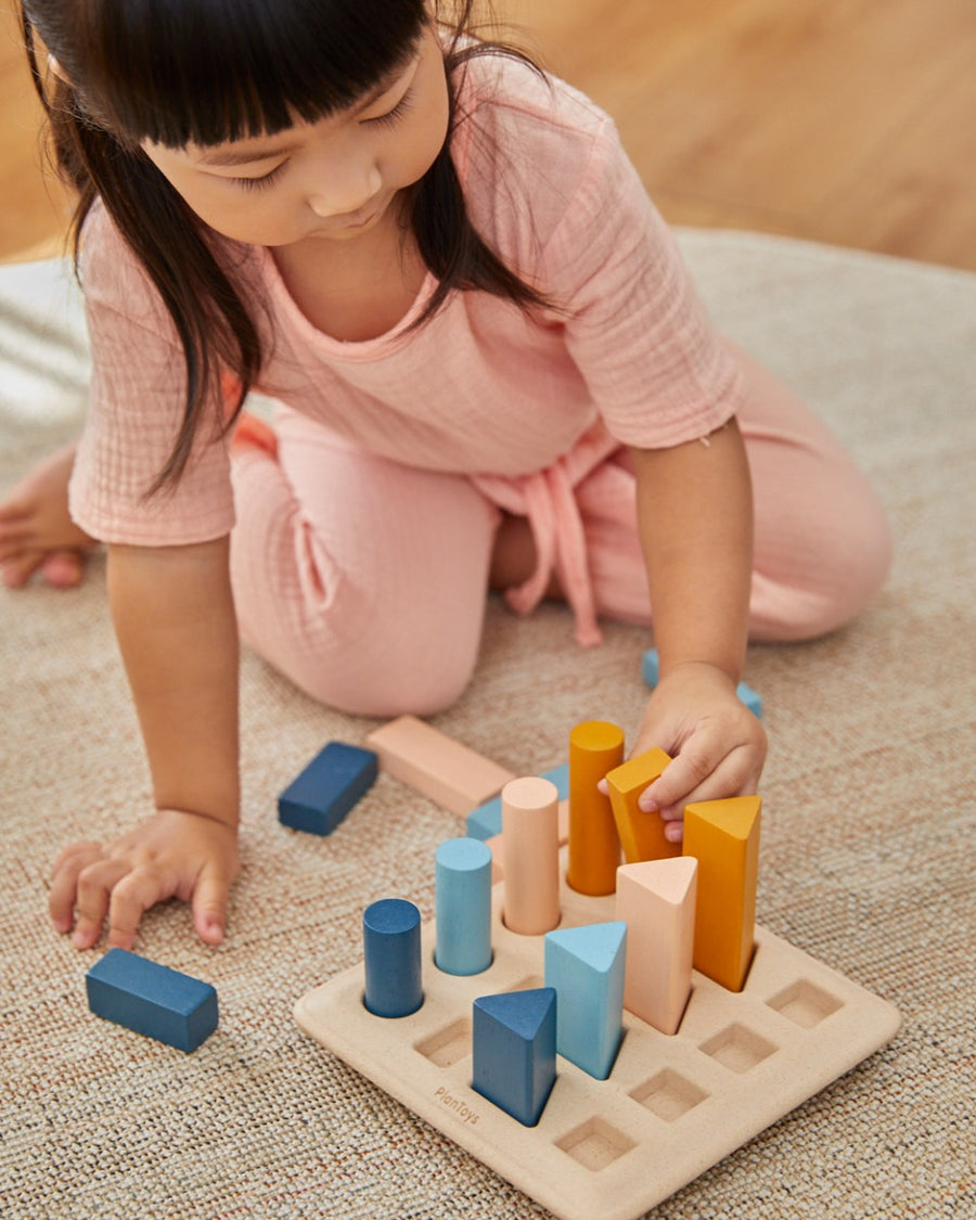 Young child crouched down placing shapes in the PlanToys wooden orchard peg board toy