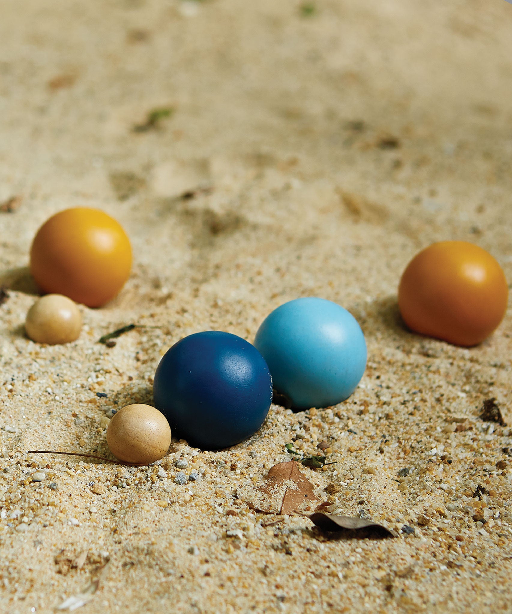 A close up of the Plan Toys plastic-free wooden petanque toy set on some sand.