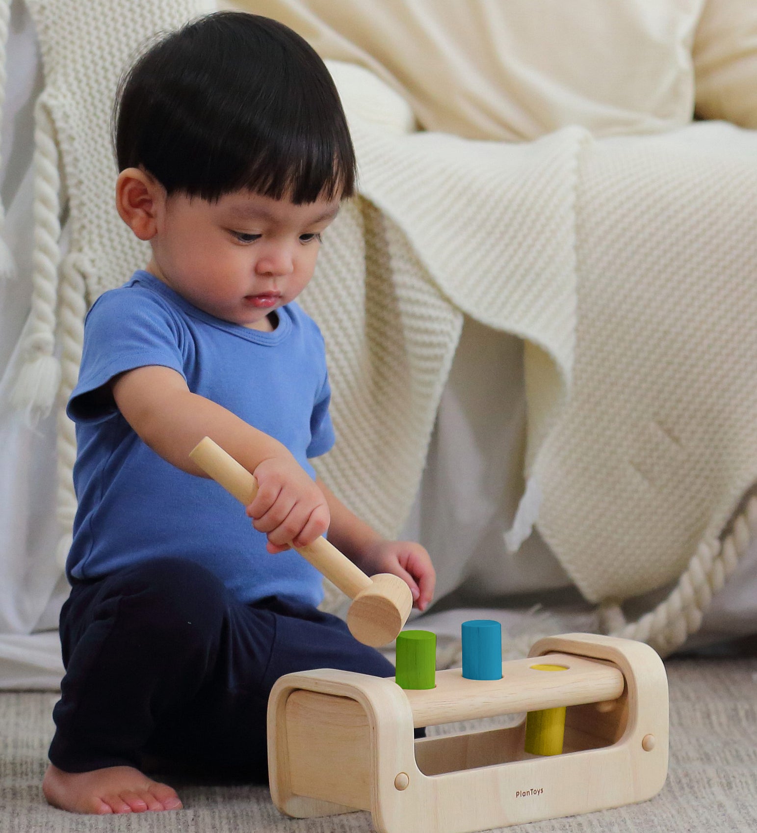 A child playing with the PlanToys Pounding Bench, and using the hammer/mallet to hammer the pegs through the holes.