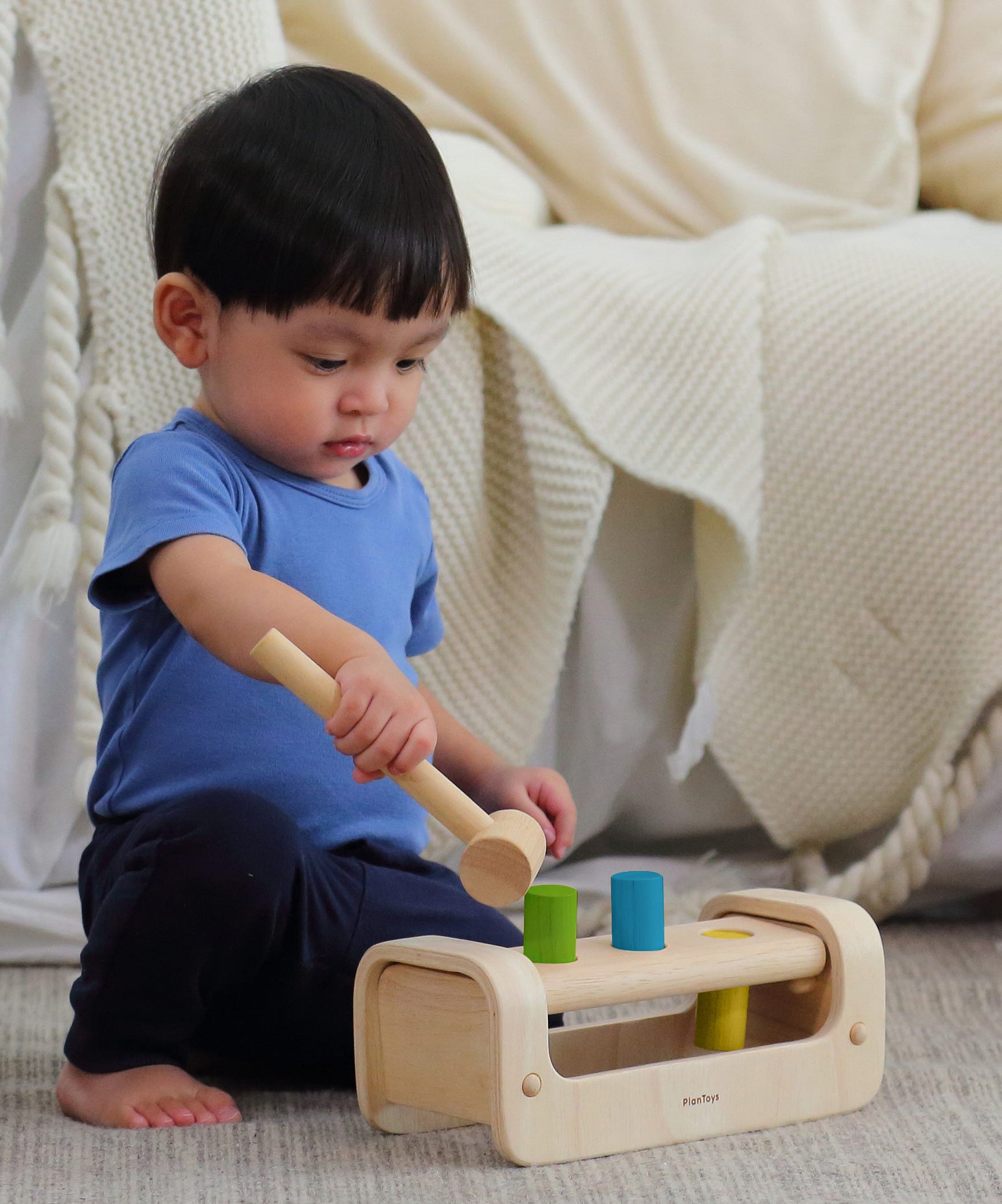 A child playing with the PlanToys Pounding Bench, and using the hammer/mallet to hammer the pegs through the holes.