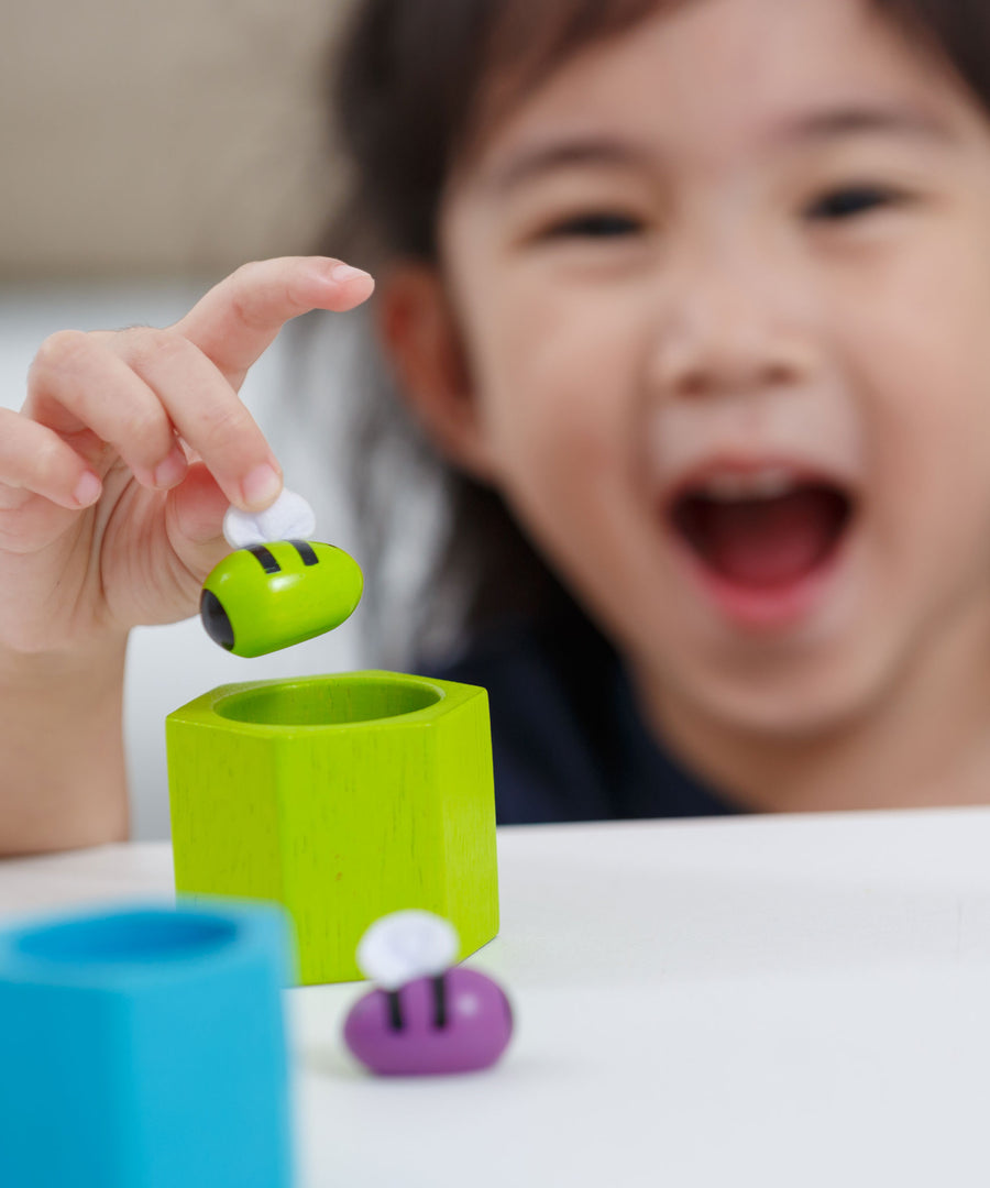 A close up of a child placing the green bee from the Plan Toys Bee Hives Rainbow set into the green hive. 