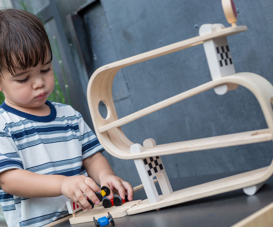 A child playing with the PlanToys Ramp Racer. The ramp racer has been placed on a PlanToys table. The child is holding the red and yellow cars. 