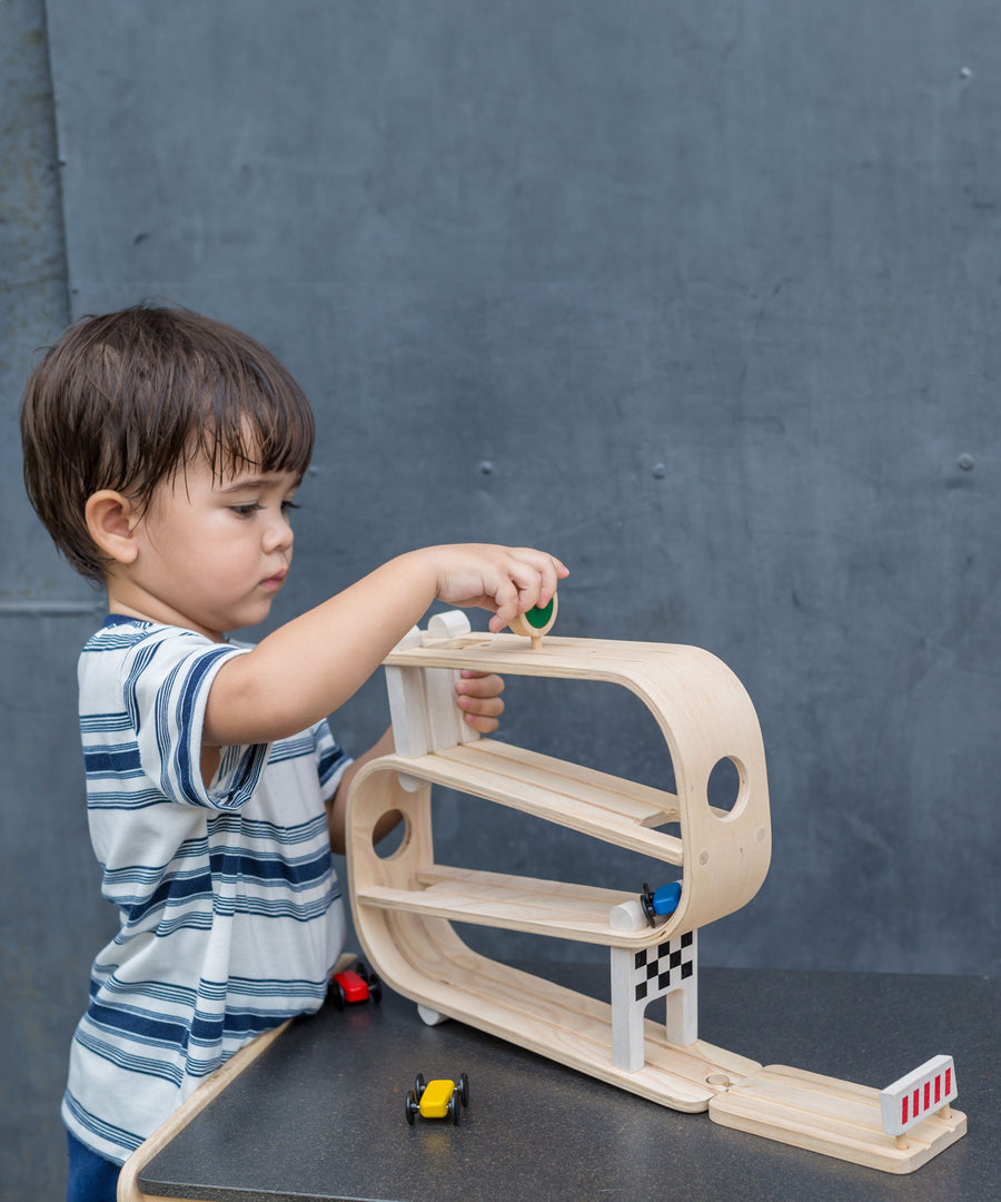 A child playing with the PlanToys Ramp Racer. The ramp racer has been placed on a PlanToys table. 