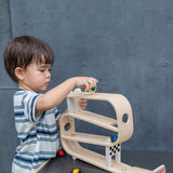 A child playing with the PlanToys Ramp Racer. The ramp racer has been placed on a PlanToys table. 