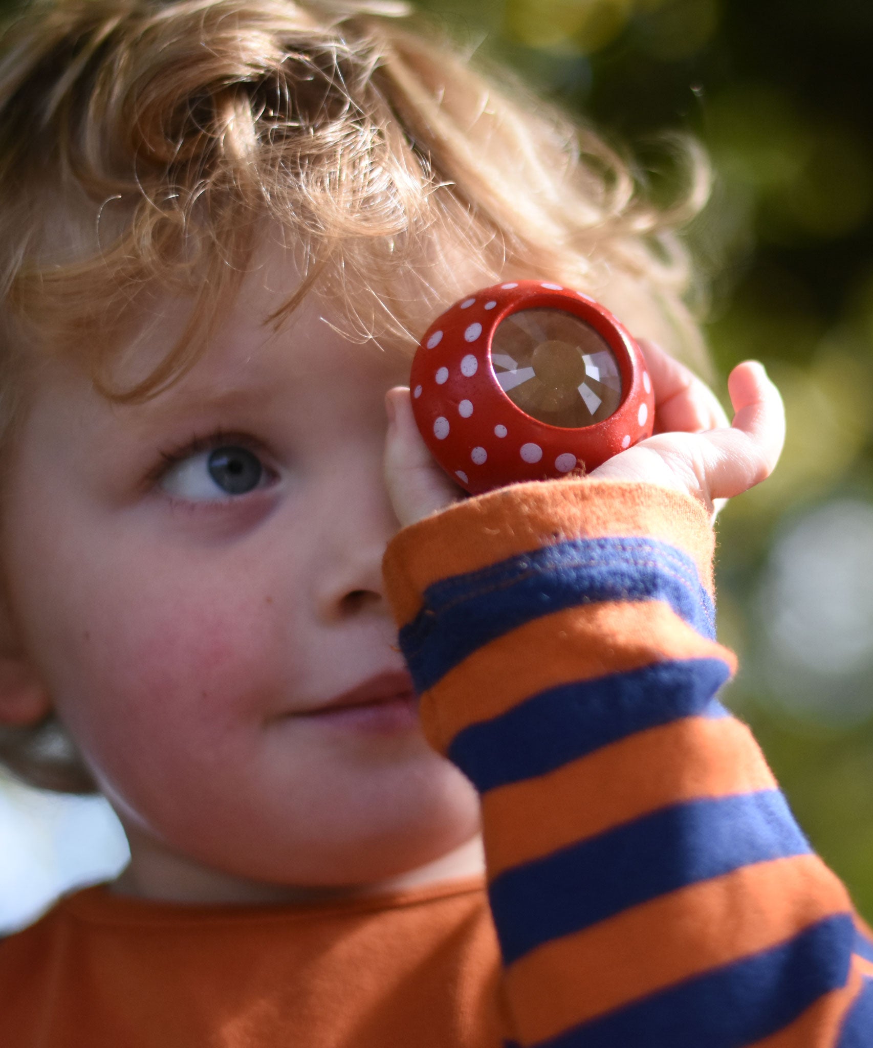 A child holding a red PlanToys Mushroom Kaleidoscope up to their eye. 