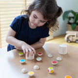 A child sitting by the table playing with the PlanToys Wooden shake and flip game.