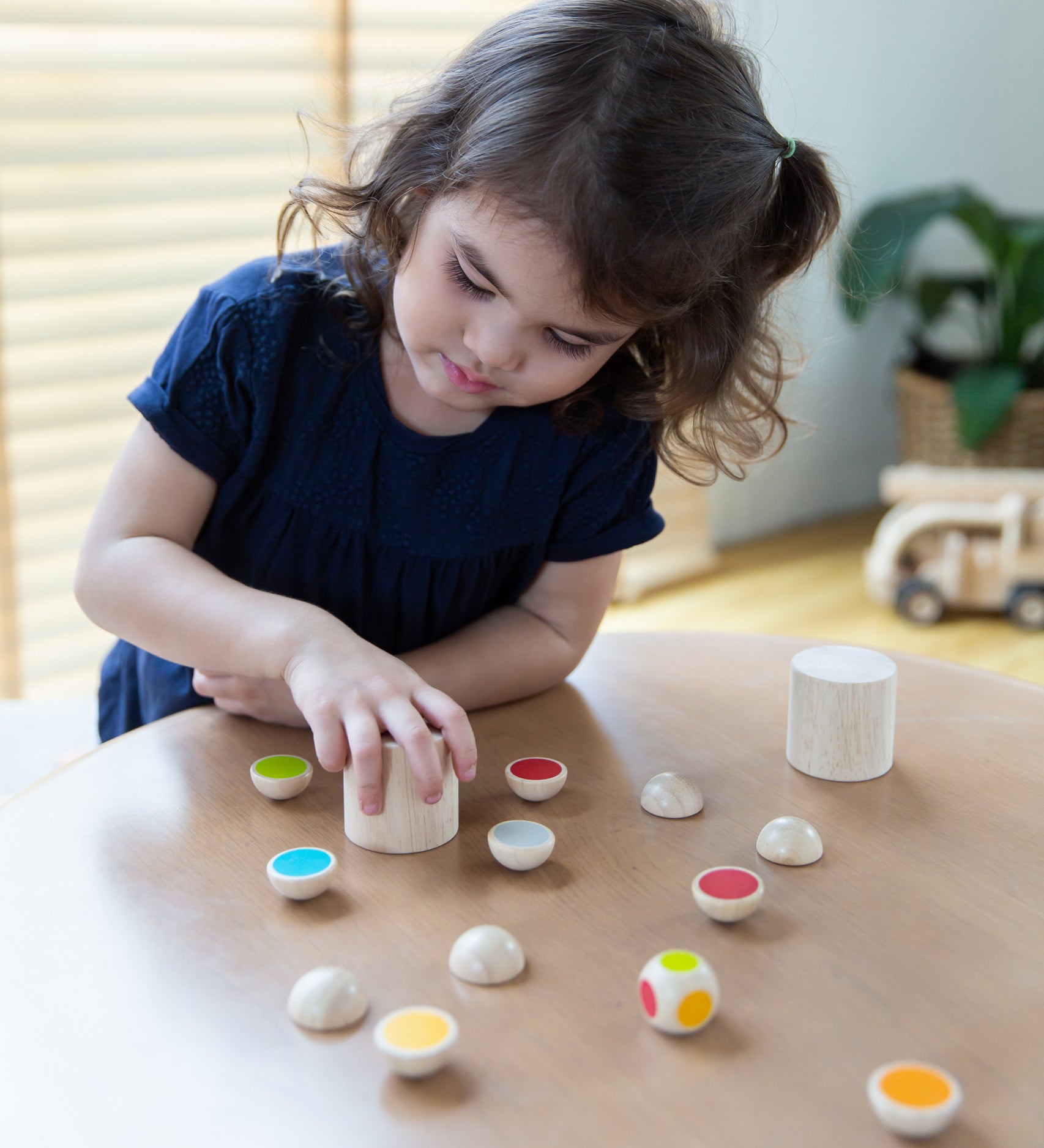 A child sitting by the table playing with the PlanToys Wooden shake and flip game.